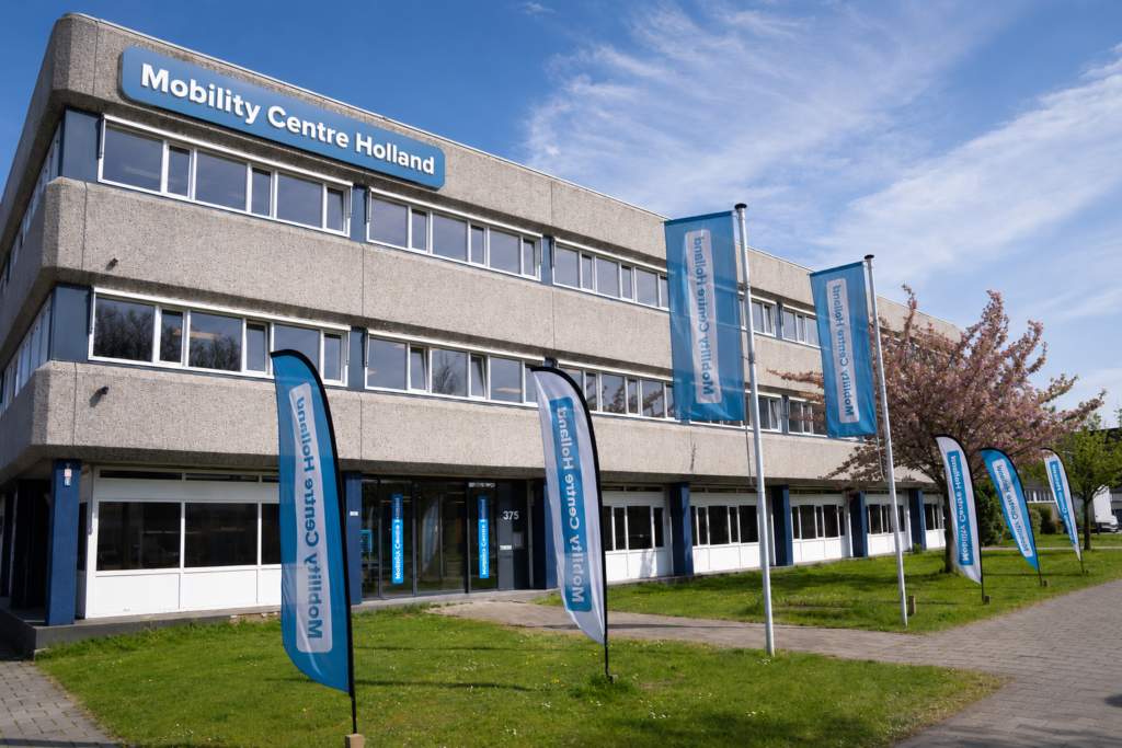 Voorgevel van het kantoorgebouw van Mobility Centre Holland aan de Hargalaan 375 in Schiedam, met blauwe gevelreclame en meerdere beachvlaggen.